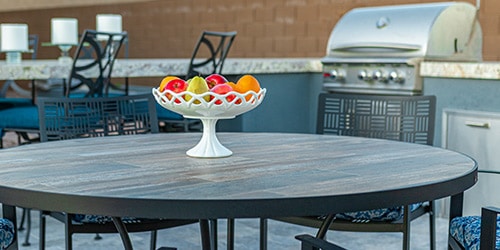 An outdoor setting with table and barbecue grill in the background