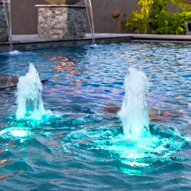 Pool water features known as gushers with blue LED lights under them