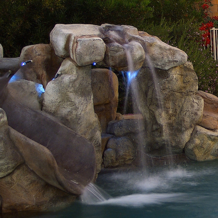 A grotto with a natural rock waterslide in a luxury pool