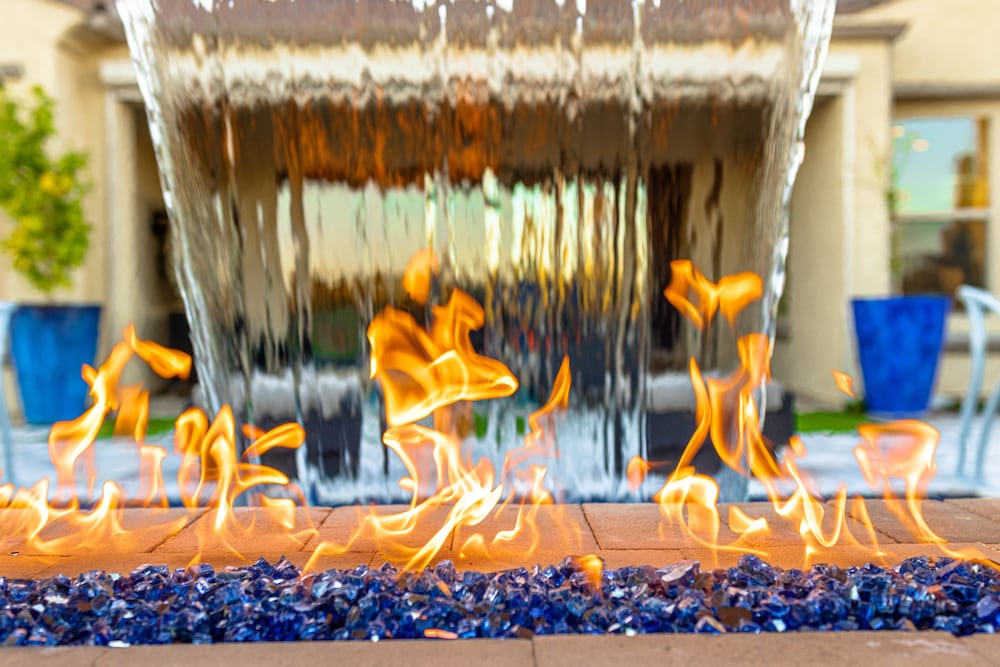 A pool fire feature with blue glass fragments and water flowing over the back