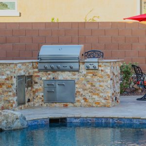 An outdoor kitchen with a BBQ grill next to a pool