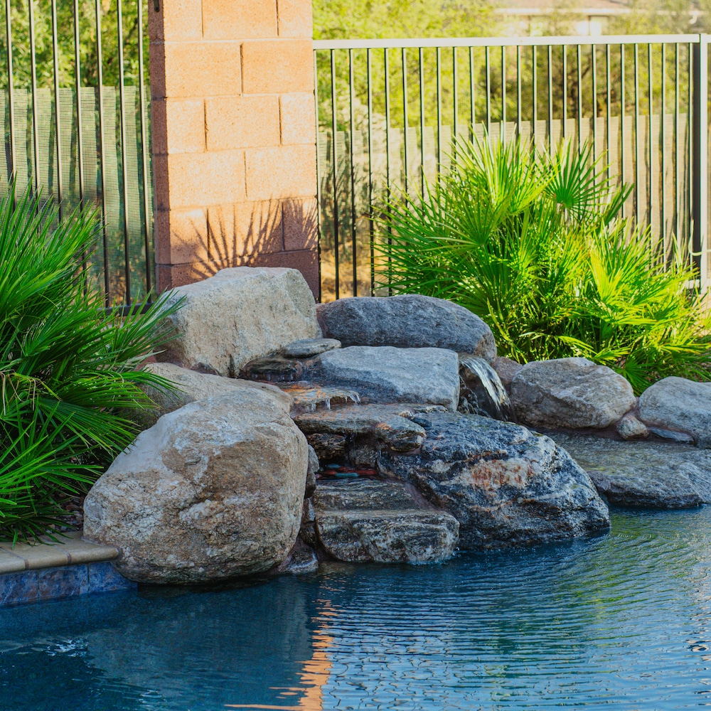 A pool with a tropical landscape featuring palm trees and a waterfall